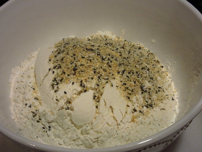 Everything seasoning blend being added to flour in a bowl.