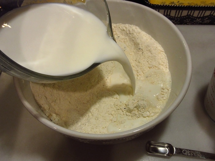 Milk being added to a bowl of flour.