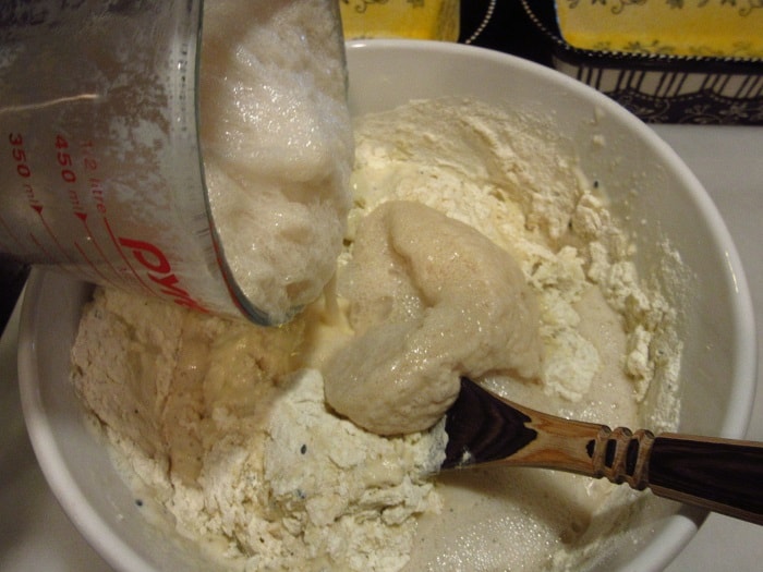 Foamy yeast being added to a bowl of dough.
