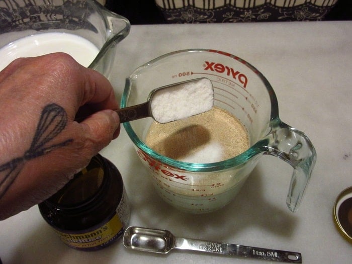 Sugar being added to a measuring cup with yeast and water.