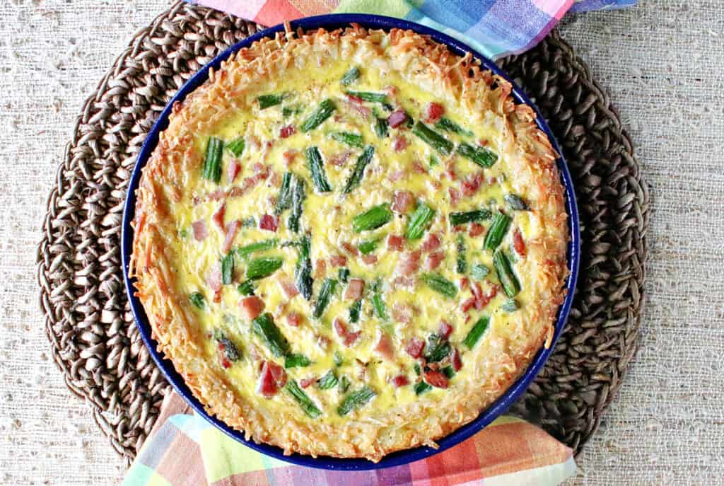 A direct overhead photo of a whole Ham and Asparagus Quiche with a hash brown crust and colorful napkins.