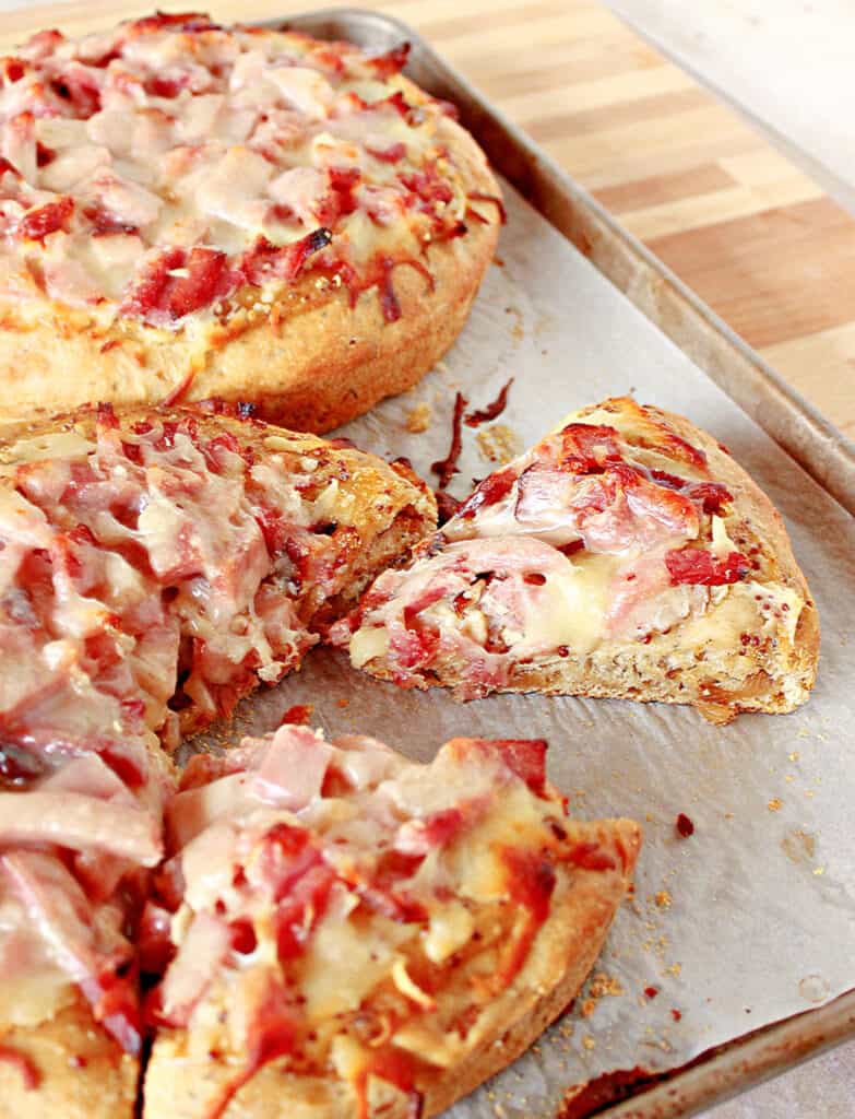 A vertical image of a sliced Leek and Onion Focaccia on a baking sheet with melted cheese and ham.