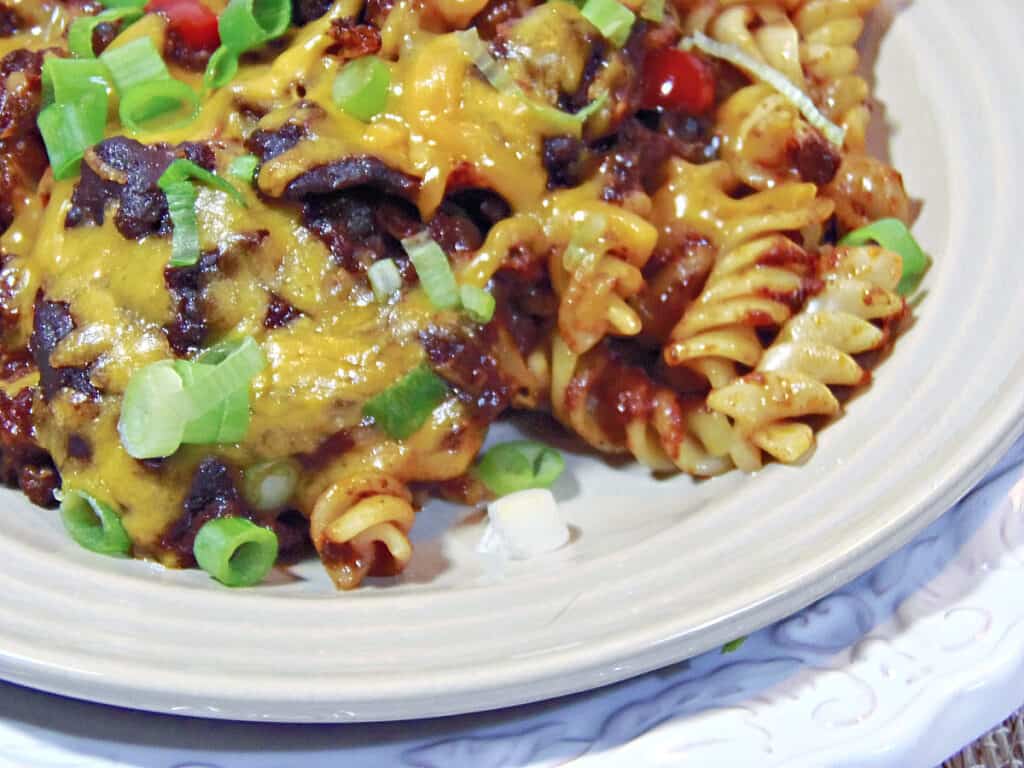 A closeup horizontal photo of Mexican Mac and Cheese Pasta with rotini noodles, melted cheese, beans, and scallions.