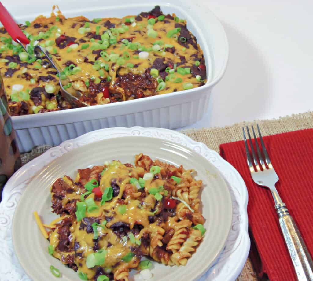 A plate filled with Mexican Mac and Cheese Casserole in the foreground and a filled white 13 x 9 casserole dish in the background.