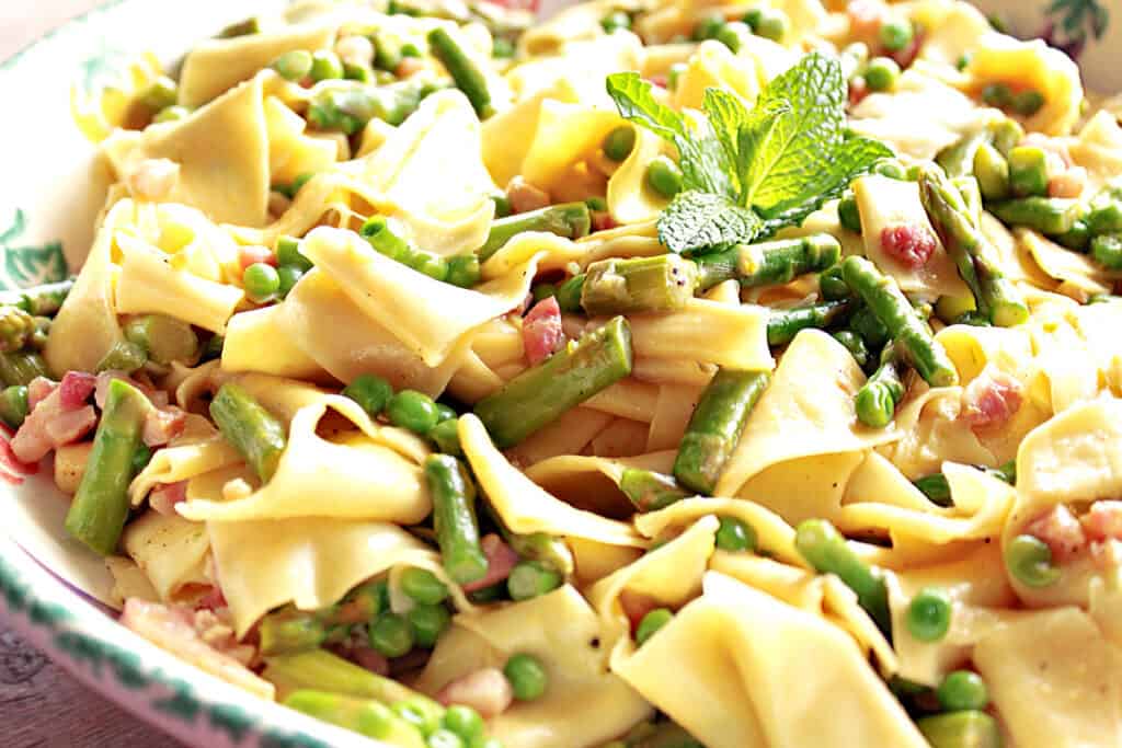 A closeup horizontal photo of a bowl filled with Pappardelle with Spring Vegetables like peas and asparagus.