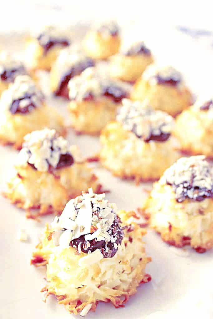 A vertical closeup photo of a tray of Almond Joy Coconut Macaroons along with a chocolate dollop and chopped nuts.