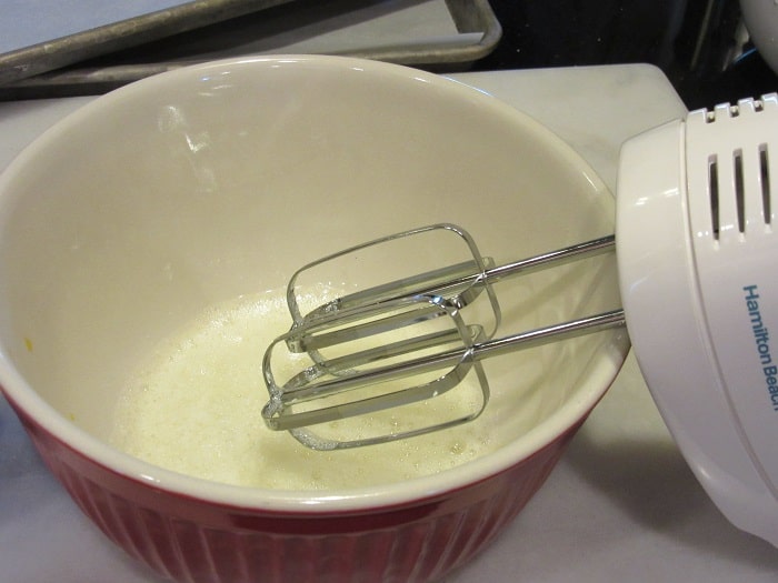 A hand mixer in a bowl of egg whites.
