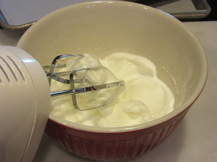 Fluffy egg whites in a bowl with a hand mixer.