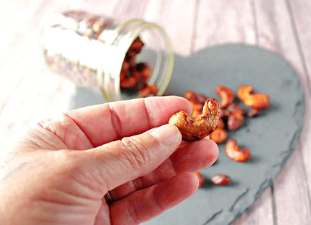 A closeup horizontal photo of a hand holding a Browned Butter Roasted Cashew with smoked paprika.