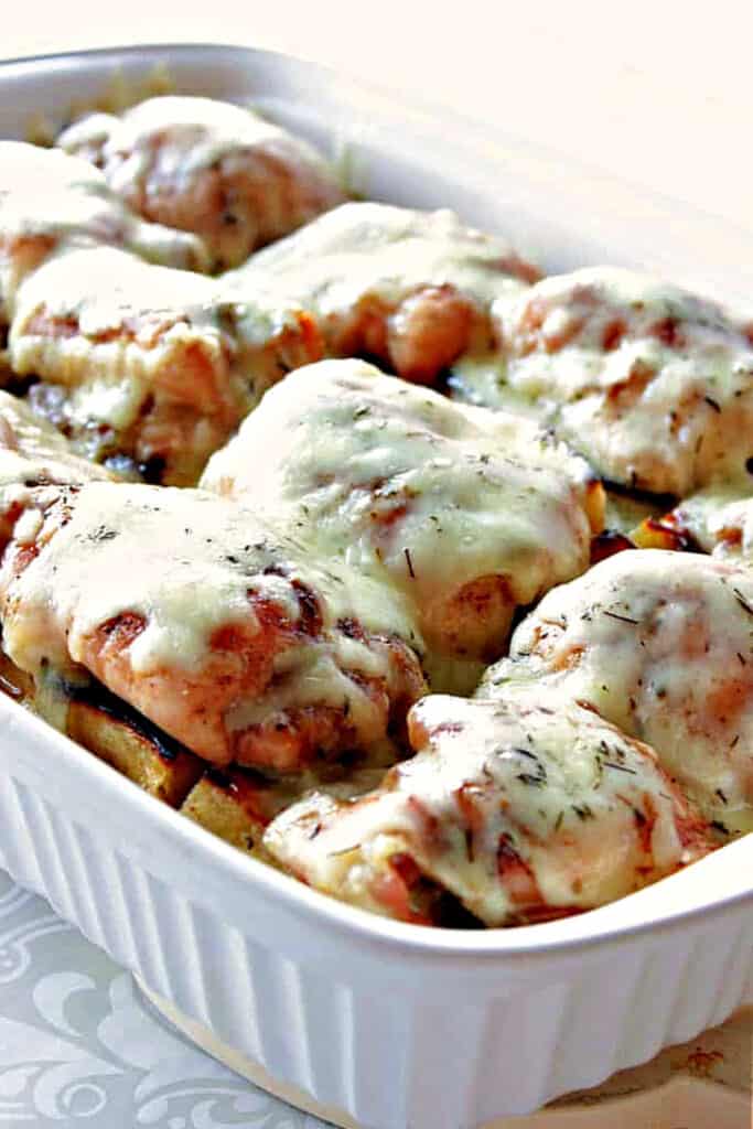 A vertical photo of a white 9x13 baking dish filled with French Onion Chicken thighs topped with melted cheese.