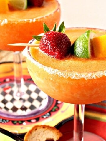 Two orange Frozen Mango and Strawberry Margarita's with fruit garnish and salt.