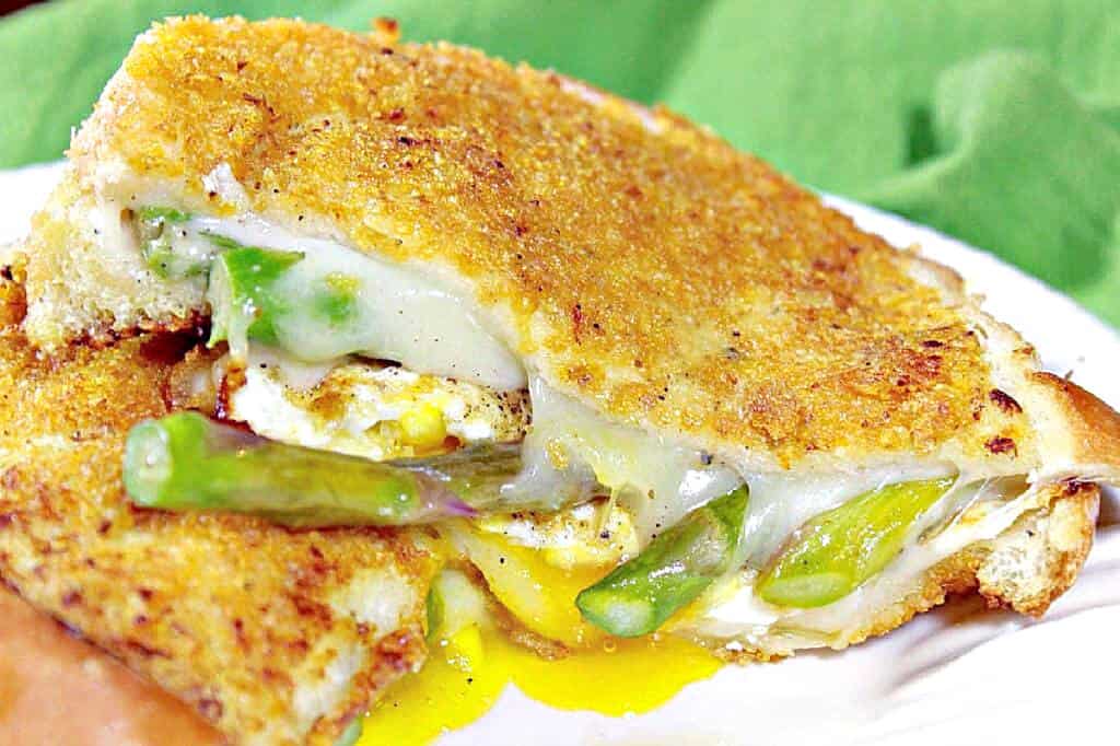 A closeup horizontal photo of the inside of a Grilled Cheese Breakfast Sandwich with runny egg yolk, melted cheese, and asparagus spears.