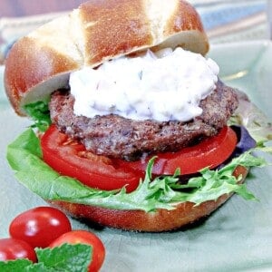 A Lamb Burger with lettuce and tomato on a green plate.