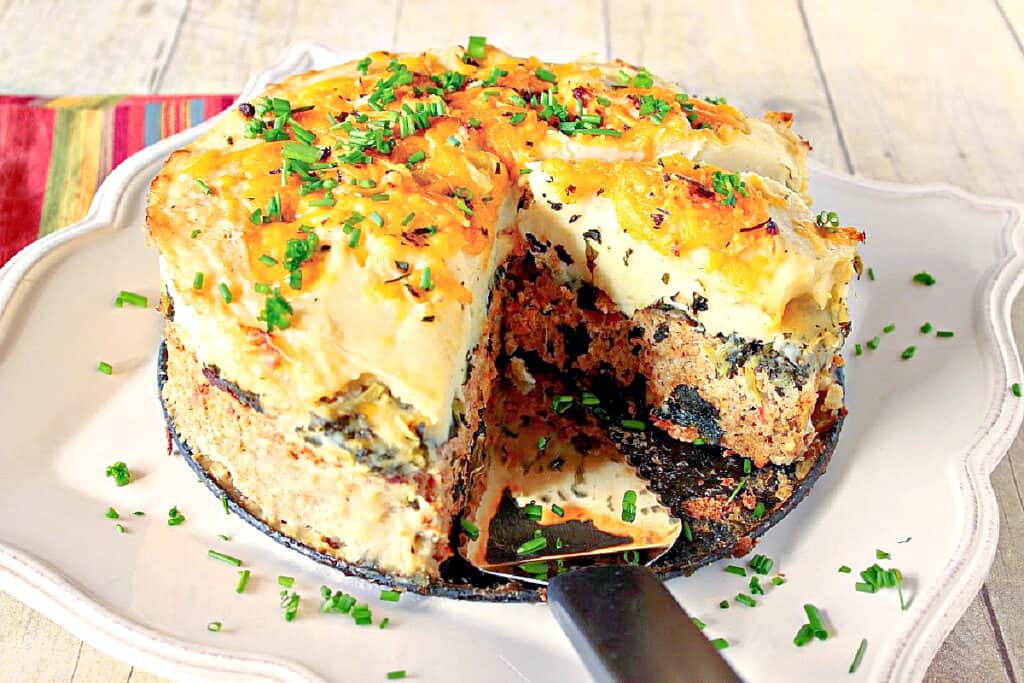 A photo of a Layered Turkey Meatloaf with a big slice taken out sitting on a pretty square white platter.