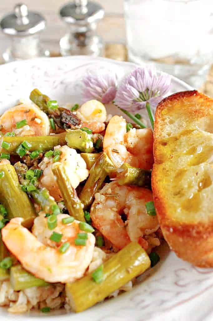 A vertical closeup photo of Shrimp and Asparagus along with chives and garlic bread.