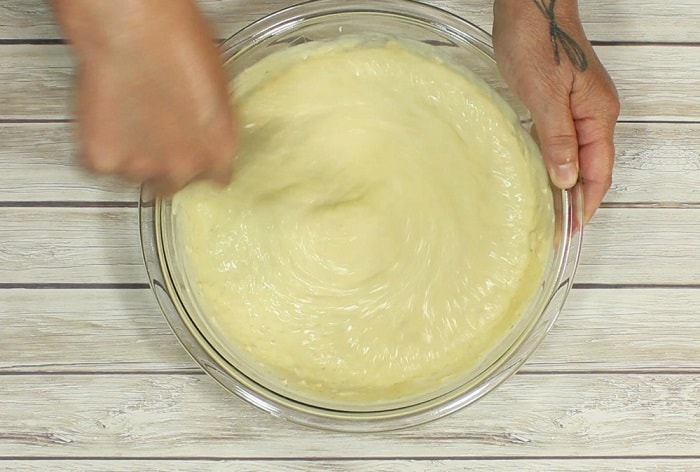 A hand whipping Alfredo sauce.