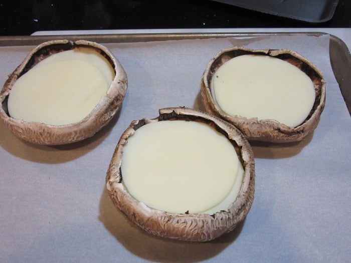 Slices of provolone cheese in large portobello mushroom caps.