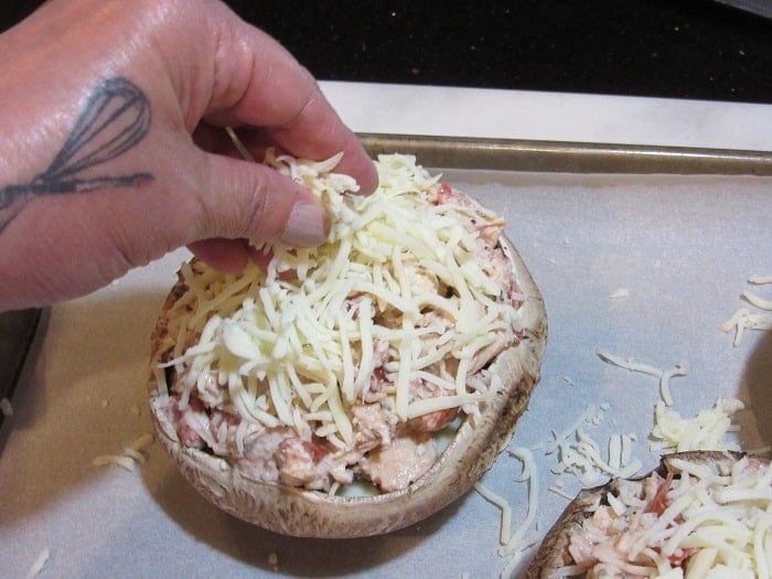 Shredded mozzarella cheese being added to a stuffed portobello mushroom.