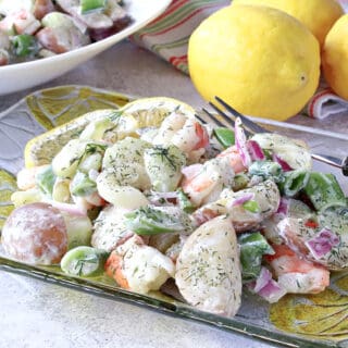 A glass plate filled with Dilled Cucumber Salad with Shrimp along with a fork and lemons in the background.