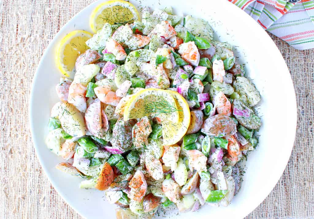 A direct overhead image of Dilled Cucumber Salad with Shrimp in a round white bowl topped with dill and lemon slices.