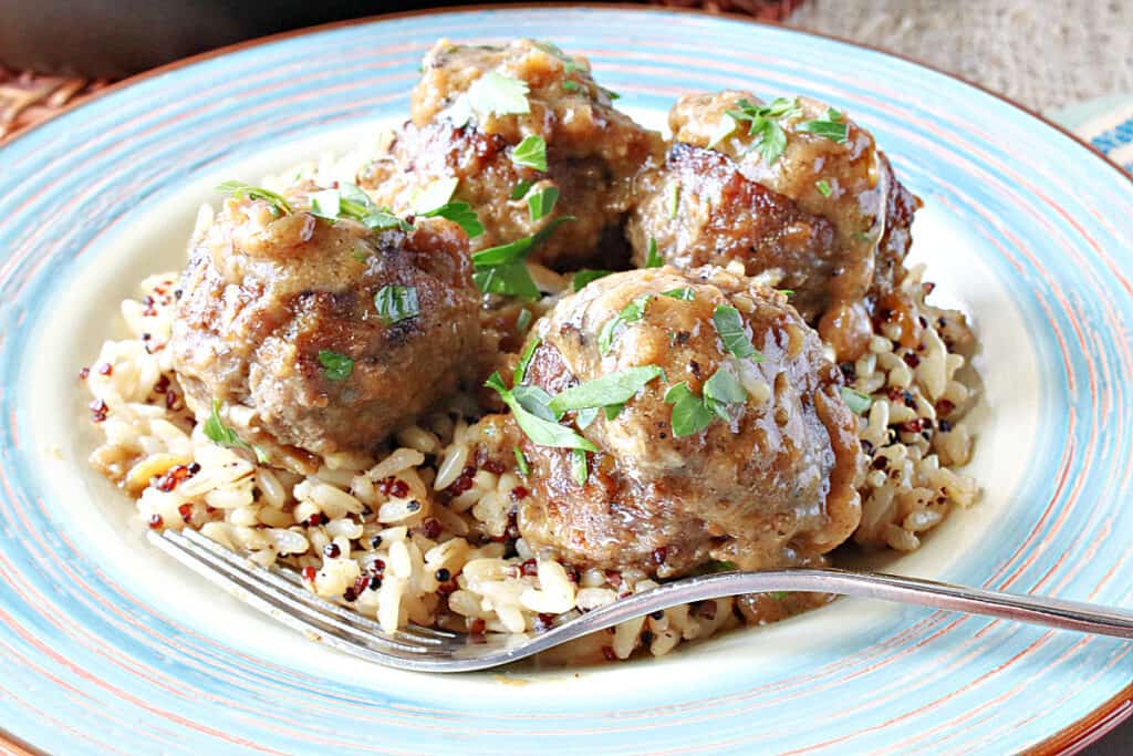 A plate filled with quinoa and rice and topped with Pork Meatballs with Apple and Onion along with a brown sauce and parsley.