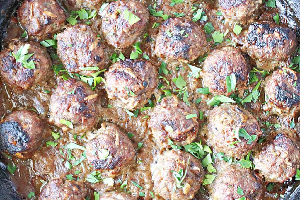 Overhead closeup image of Pork Meatballs with Apple and Onion in a skillet with chopped parsley as garnish.