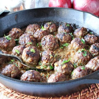 A cast iron skillet filled with Pork Meatballs with Apple and Onion and a serving spoon.