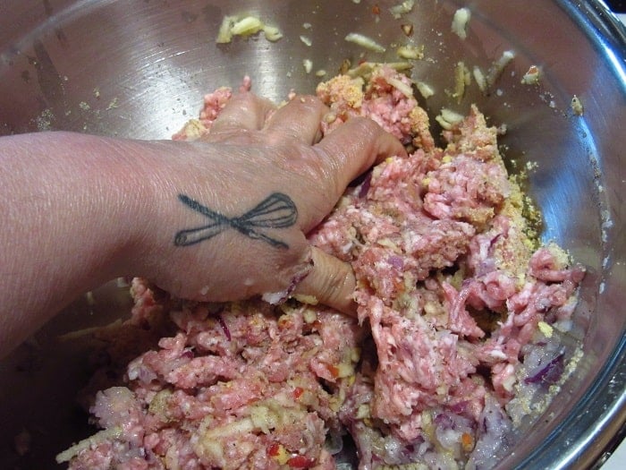 A hand mixing ground pork for meatballs.