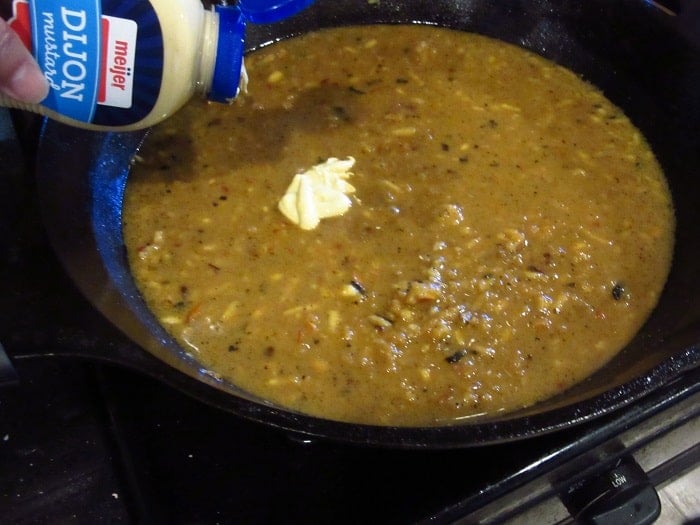 Dijon mustard being added to a sauce in a cast iron skillet.
