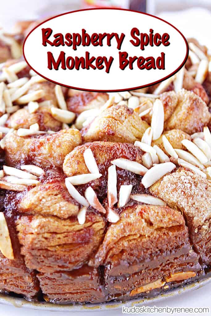 A vertical closeup along with a title text overlay graphic for Raspberry Spice Monkey Bread with a cinnamon sugar coating, raspberry jam, and almonds.