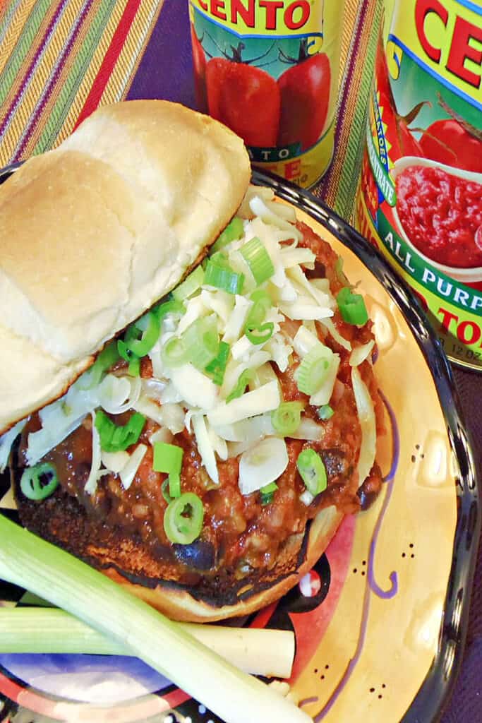 An overhead closeup photo of a Sloppy Jose Pork Sausage Sandwich topped with cheese and scallions along with a toasted bun.