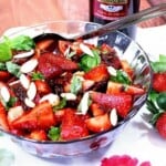 A glass bowl filled with Strawberry, Tomato, and Basil Salad along with a serving spoon.