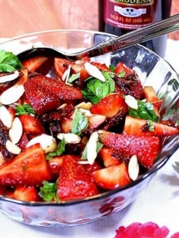 A glass bowl filled with Strawberry, Tomato, and Basil Salad along with a serving spoon.