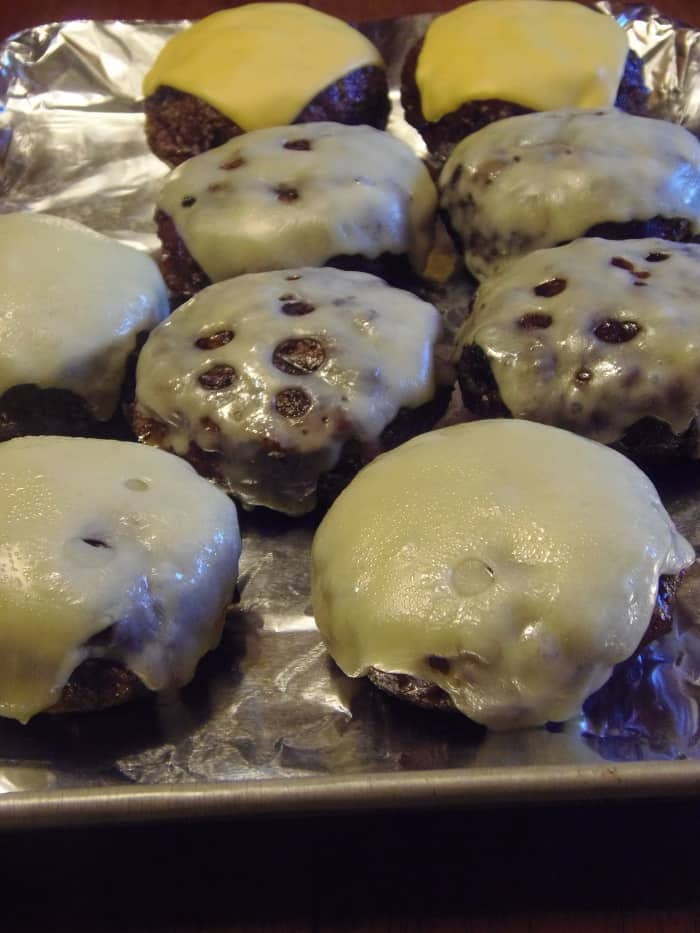 A vertical closeup of a bunch of cheese covered burgers stuffed with caramelized onions.