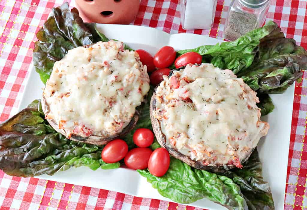 An overhead horizontal photo of two Chicken Parmesan Stuffed Portobellos on a white rectangular plate with lettuce leaves and grape tomatoes.