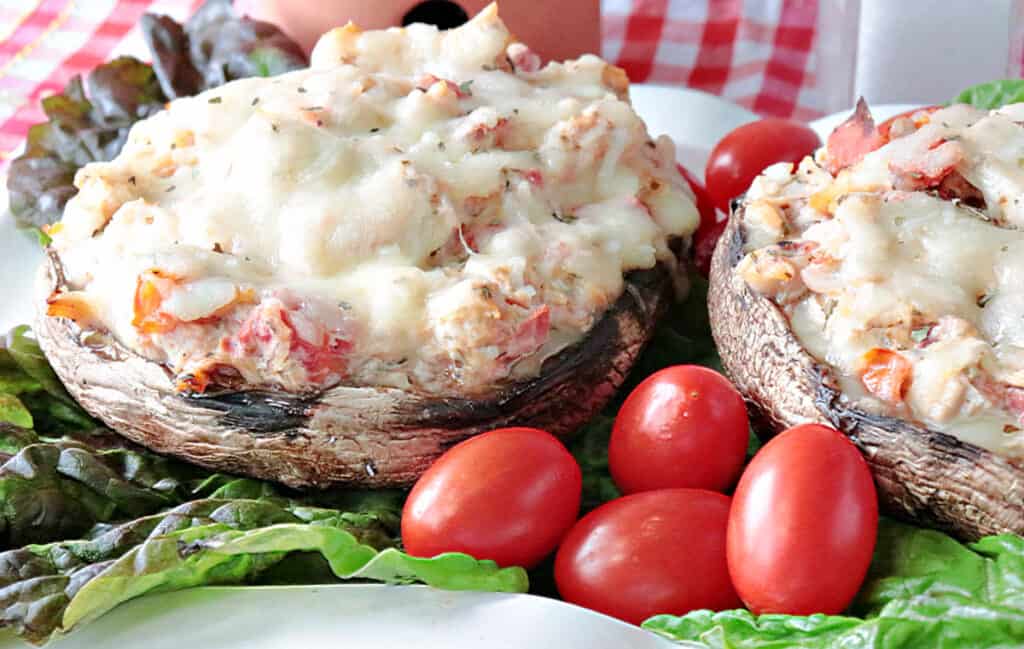 A closeup horizontal photo of two Chicken Parmesan Stuffed Portobellos on a plate with melted cheese and tomatoes.