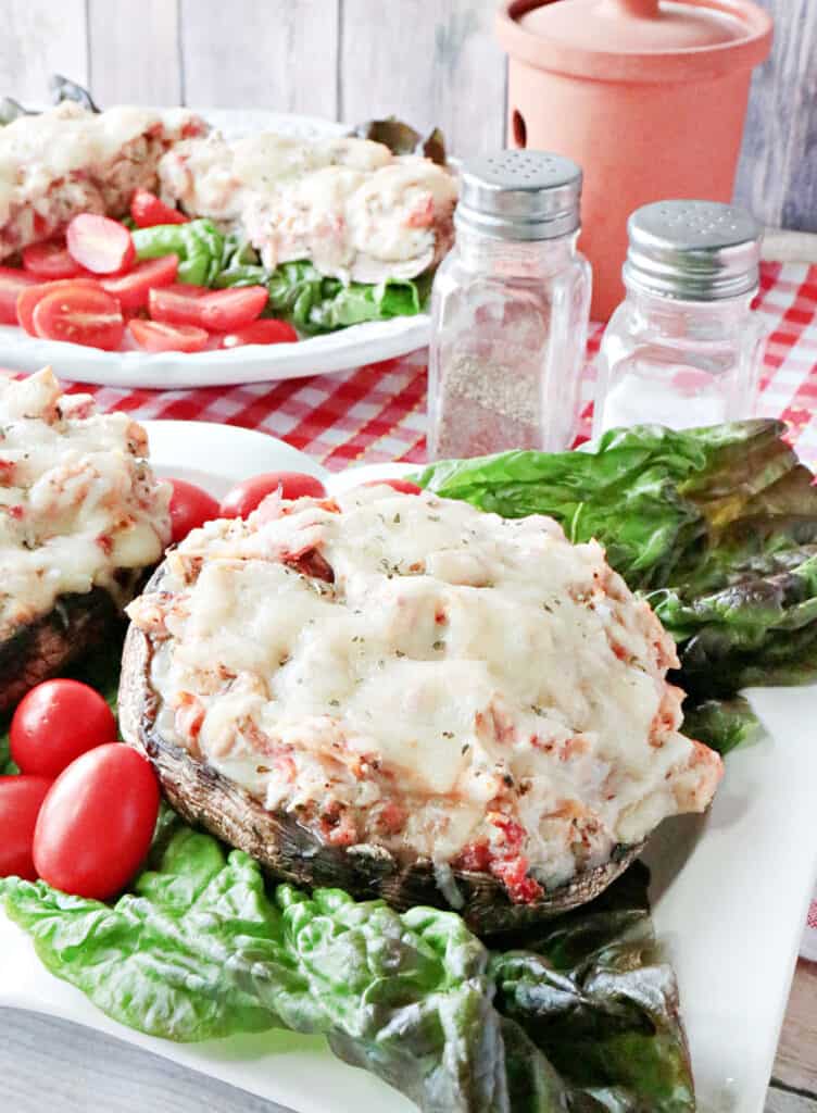 A closeup vertical photo Chicken Parmesan Stuffed Portobellos, one in the foreground and one in the background cut in half.