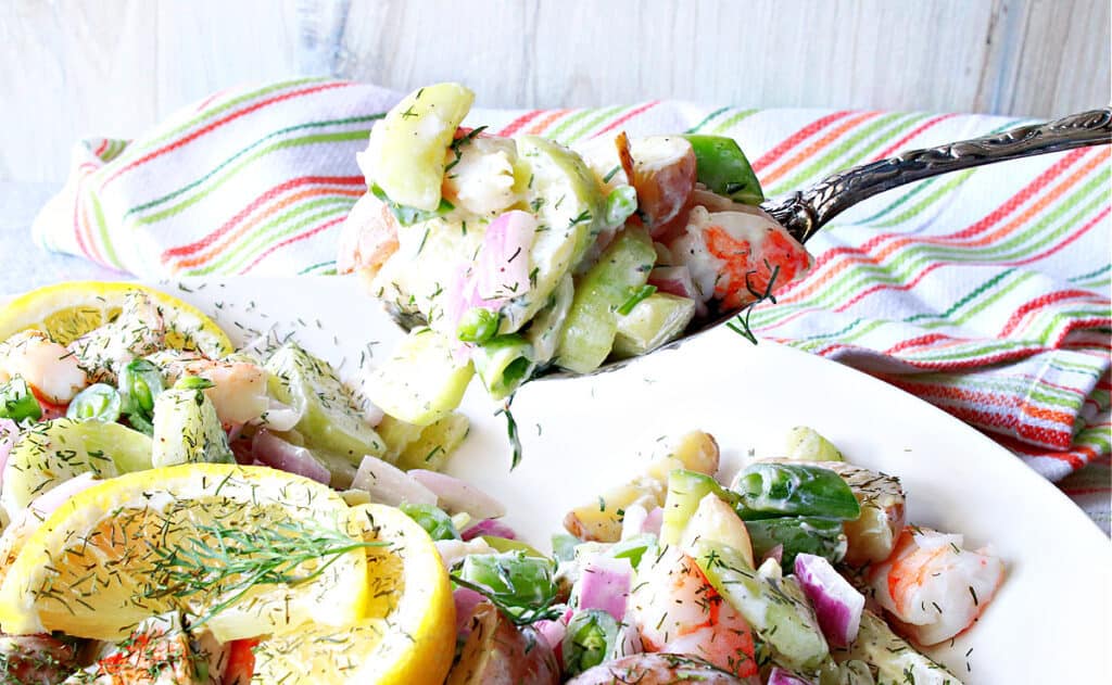 A closeup horizontal image of a spoonful of Dilled Cucumber Salad with Shrimp with a colorful napkin in the background.