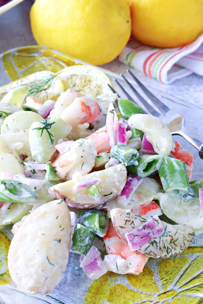 A vertical closeup of a serving of Dilled Cucumber Salad with Shrimp on a glass plate with lemons and a fork.