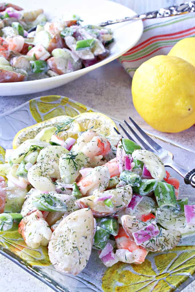 A serving of Dilled Cucumber Salad with Shrimp on a pretty glass plate with a fork and lemons in the background.