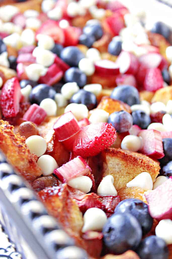 A closeup vertical image of Red, White and Blue Bread Pudding with strawberries, rhubarb, blueberries, and white chocolate chips.