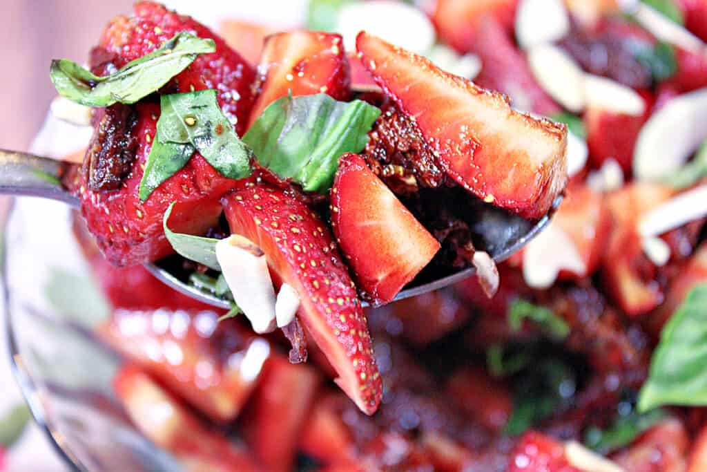 A horizontal photo of a spoon filled with Strawberry Basil Salad with almonds.