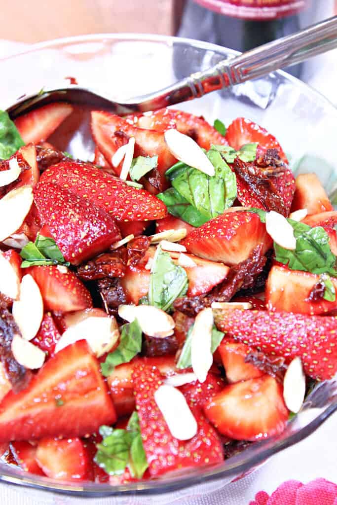 A vertical closeup image of sliced strawberries in a Strawberry Basil Salad with sun dried tomatoes and sliced almonds.