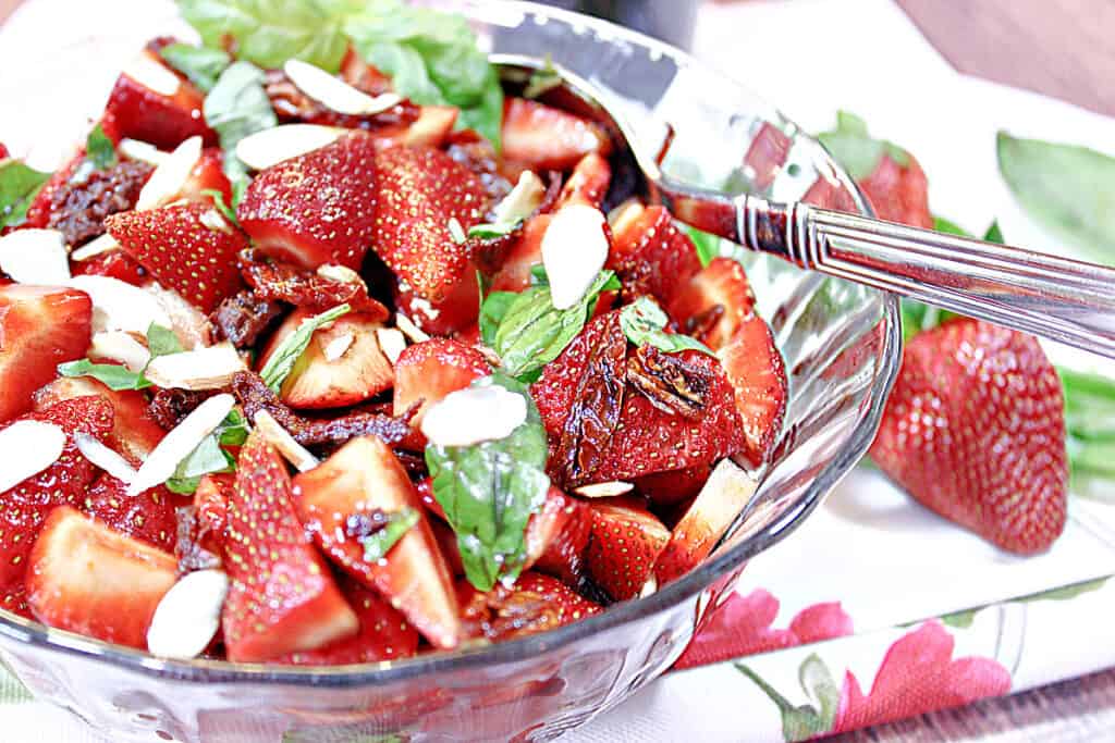 An offset photo of a Strawberry Basil Salad in a glass bowl with a spoon.