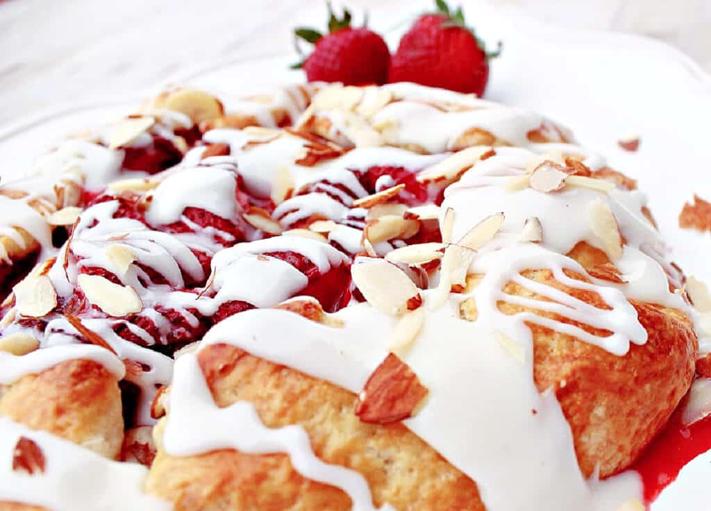 A super closeup horizontal image of a homemade Strawberry Crostata with a white sugar glaze and fresh strawberries as a garnish.