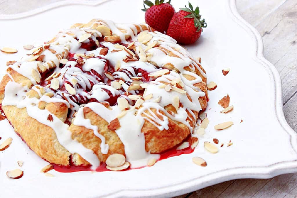 An offset horizontal photo of a Strawberry Crostata on a pretty square white plate with fresh strawberries as garnish.