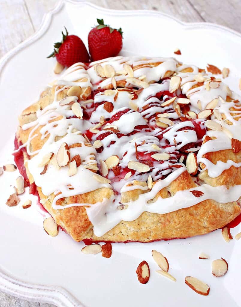 A vertical closeup of a Strawberry Crostata with an almond glaze on a white plate with slivered almonds.