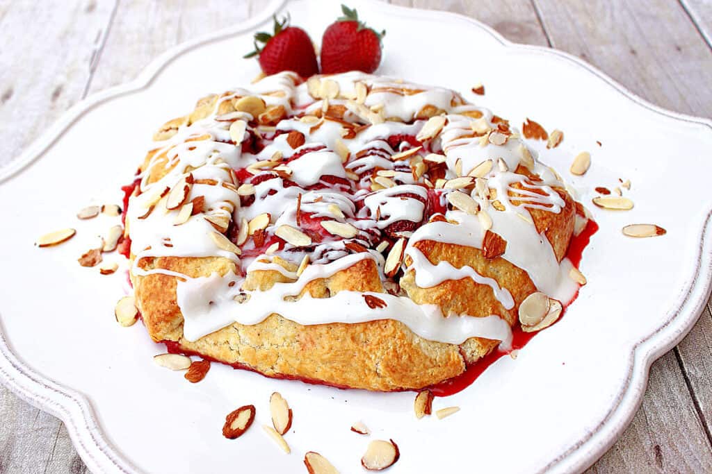 A Strawberry Crostata on a pretty white square plate with a almond glaze and sliced almonds.