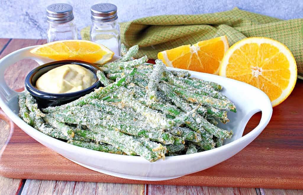 A white oval bowl filled with Everything Green Bean Fries along with an orange dipping sauce and fresh oranges.