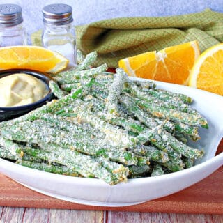 A white oval bowl filled with Everything Green Bean Fries along with an orange dipping sauce and fresh oranges.